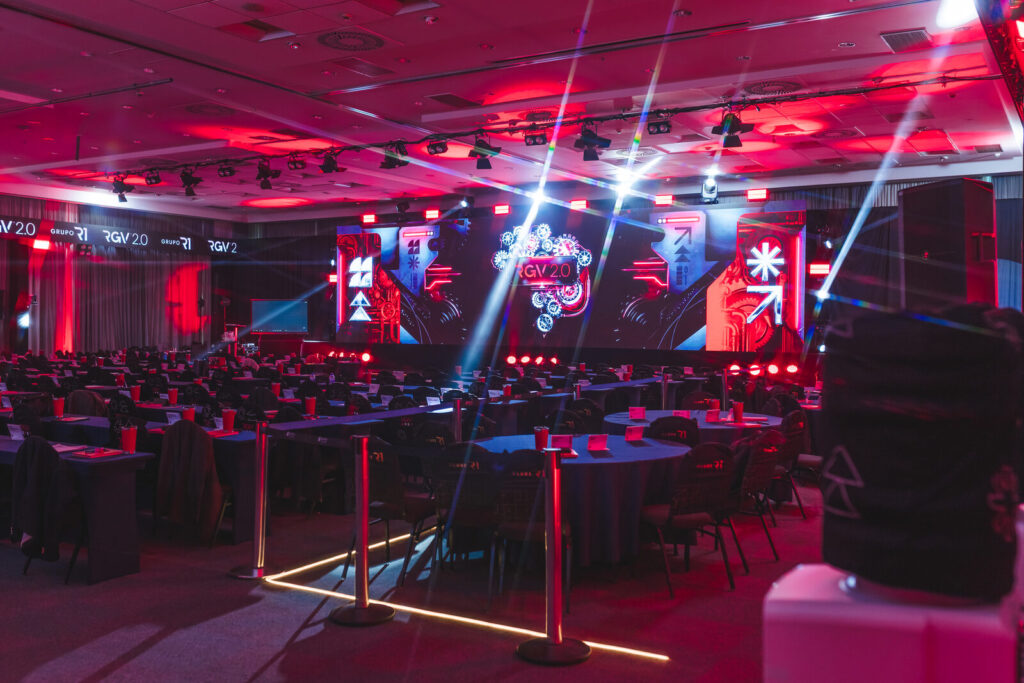 Salão do evento corporativo RGV 40 com iluminação cênica e mesas, estrutura da Levium Eventos