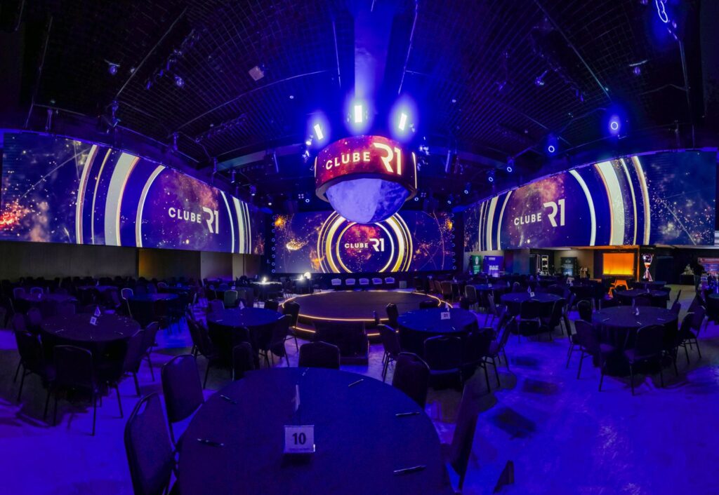 Arena com mesas ao redor do palco central e painéis de LED em volta