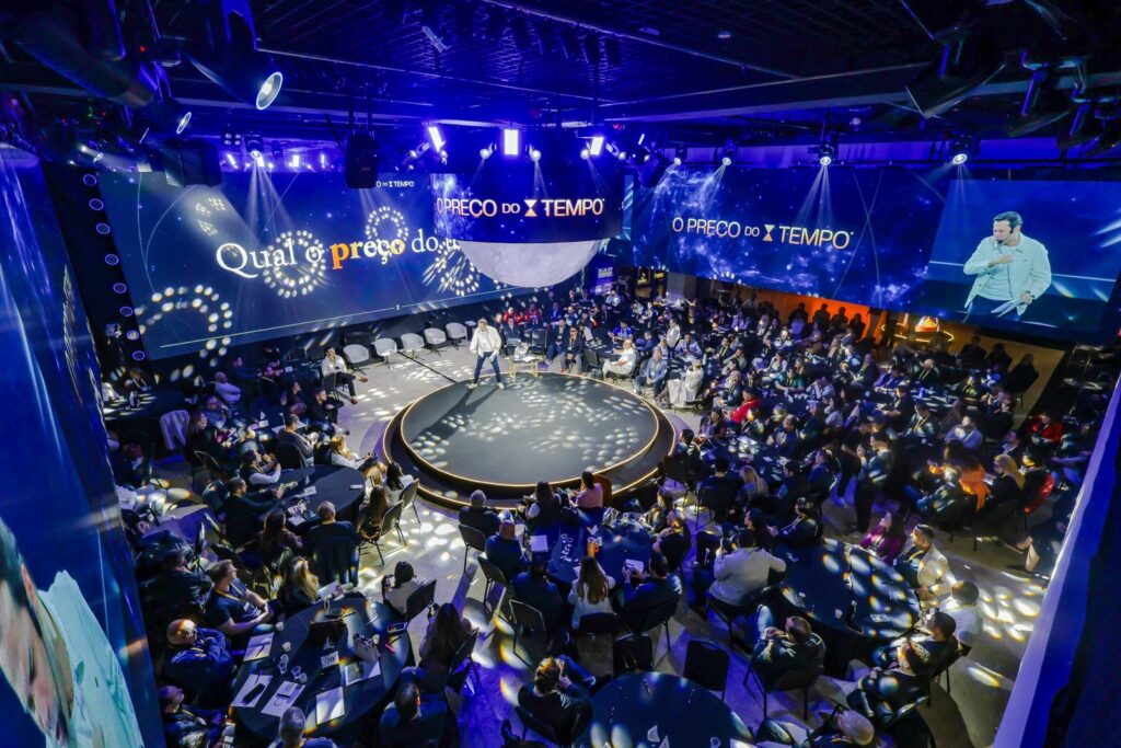 Palco central 360° do evento O Preço do Tempo, do Clube R1, com painéis de LED e plateia de empresários