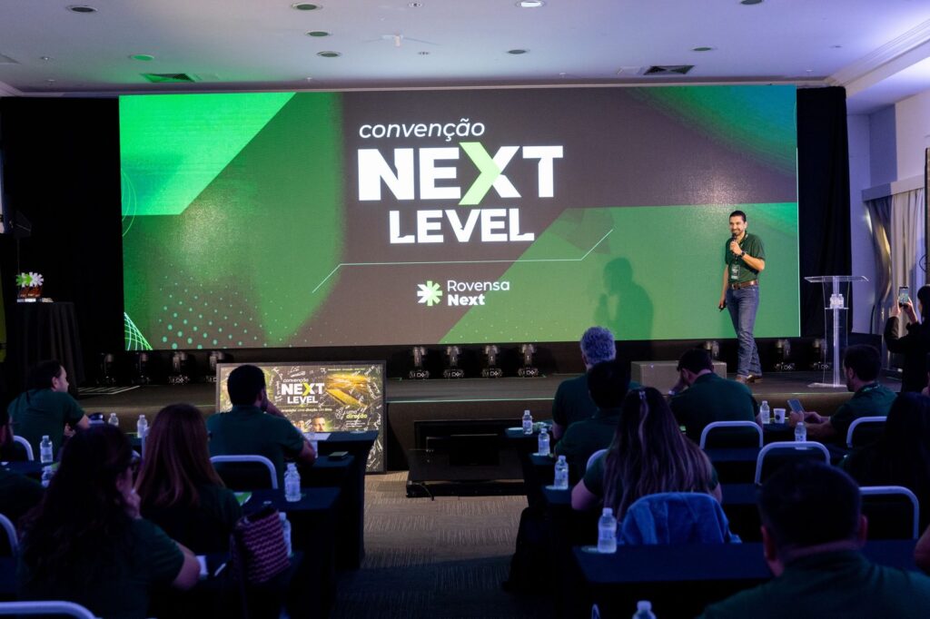 Apresentação em andamento diante do painel de LED com a identidade Next Level.
