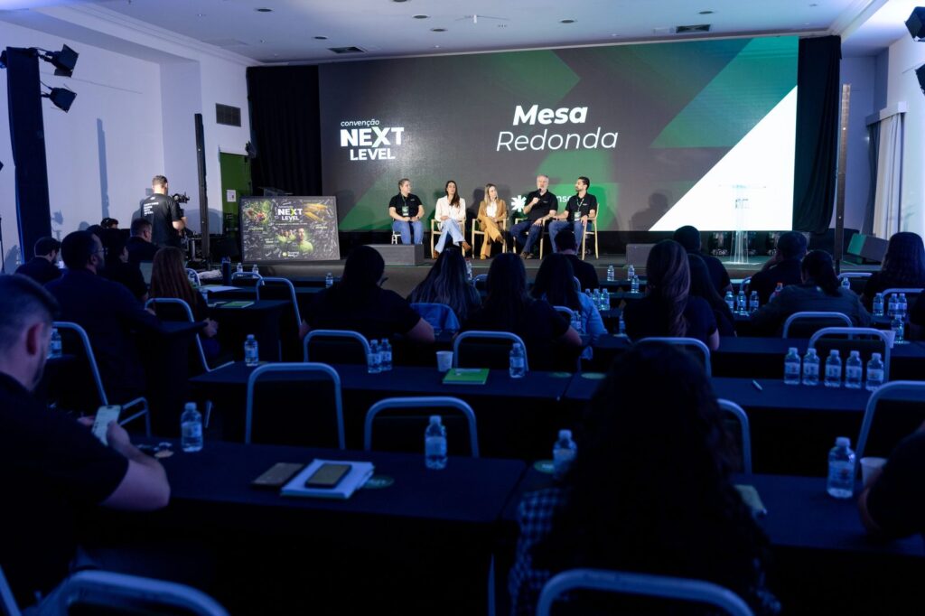 Mesa-redonda com painel de LED e público na plenária.